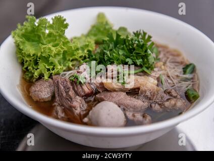 Zuppa di manzo thai chiara di riso bianco, spaghetti vermicelli con manzo brasato, polpette e verdure. Delizioso fast food di strada in Thailandia. Vista obliqua da Foto Stock