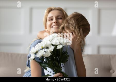 Emozionata mamma che abbracciava la piccola figlia che riceve fiori il giorno delle madri Foto Stock