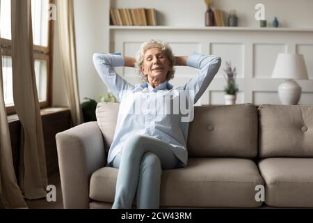 Tranquilla donna anziana con capelli grigi felice che si rilassa sul divano a casa Foto Stock