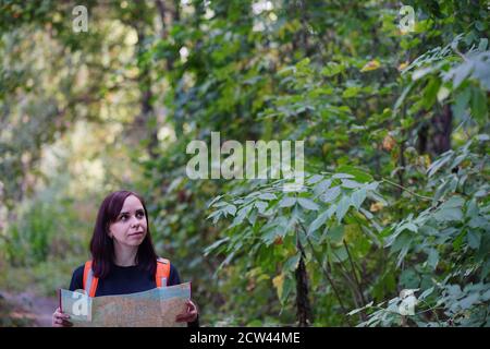 Donna in viaggio con mappa in legno. Donna con zaino che cammina in legno. Donna che trasporta lo zaino e che cammina nella soleggiata foresta autunnale Foto Stock