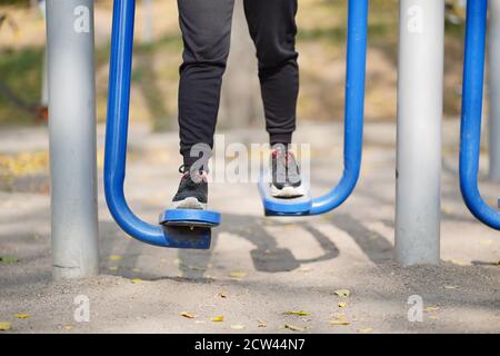 Ritratto delle gambe della donna sul simulatore di strada nel parco. Primo piano di parte del corpo di femmina che fa sport sul campo atletico nella stagione autunnale Foto Stock