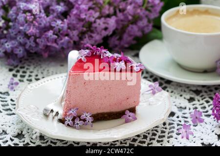 Una torta di mousse di frutti di bosco con base di cioccolato e gelatina di succo, decorata con fiori di lilla, servita con caffè. Foto Stock
