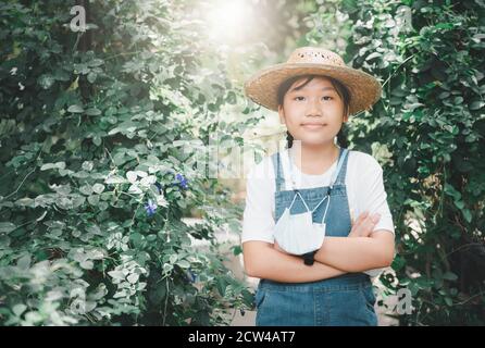 Ragazza contadina che indossa tute in denim con cappello e appende una maschera nel giardino di verdure. Foto Stock