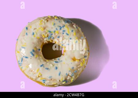 Primo piano vista della ciambella cosparsa di smalto multicolore isolato su sfondo rosa. Concetto di cibo e bevande. Foto Stock