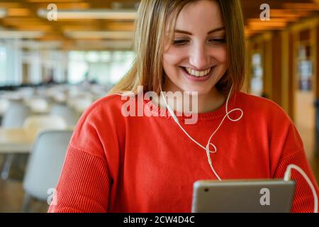 Ritratto di giovani studenti con auricolari e utilizzando tablet digitale presso la biblioteca universitaria. Concetto di istruzione. Foto Stock