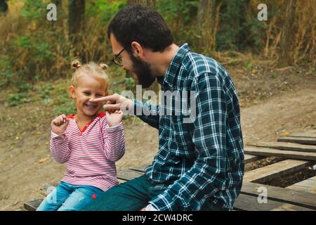 Baby e padre giocano nel parco autunnale. Papà e figlia sono seduti su un ponte di legno all'aperto. Felici momenti di infanzia in famiglia. Foto Stock