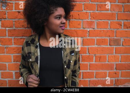 Ritratto di bella giovane afroamericana latina con capelli ricci in piedi contro muro di mattoni. Foto Stock