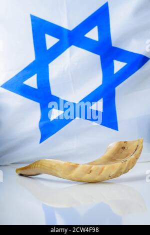Corno shofar su tavolo bianco sullo sfondo della bandiera di Israele. Shofar - Yom Kippur e Rosh Hashanah simbolo delle vacanze ebraiche. L'immagine può anche essere usata di articoli sul servizio militare dell'ebreo ortodosso nell'esercito. Foto Stock
