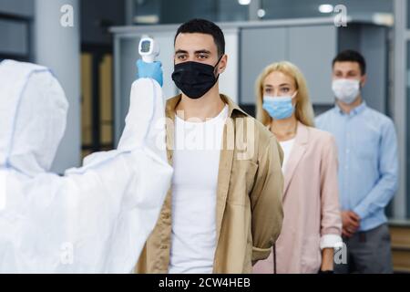 Nuovo controllo normale e della malattia del coronavirus. Medico in uniforme protettiva con termometro a infrarossi per misurare la temperatura dei lavoratori Foto Stock