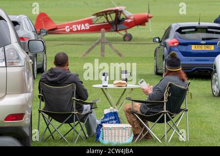 Old Warden Aerodrome, Biggleswade, Bedfordshire, UK. 27th Sep, 2020. In order to comply with the COVID-19 guidelines the Shuttleworth Collection have proceeded with their season of airshows by making them drive-in events. To avoid visitors gathering at the fence line during the flying displays they must stay within a box around their cars which are parked on the grounds facing the runway. Many have laid out picnics beside their cars. The show highlighted the centenary of de Havilland Aircraft with a large number of historic planes taking part. People with camping table and chairs Foto Stock