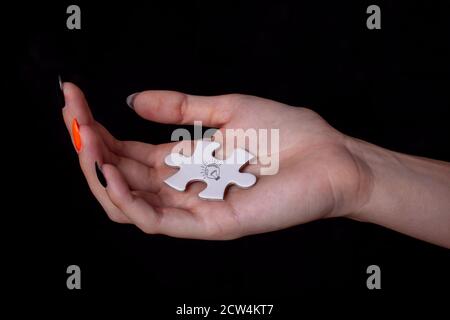 Mano della donna che tiene un elemento di puzzle bianco isolato su sfondo nero. Foto Stock