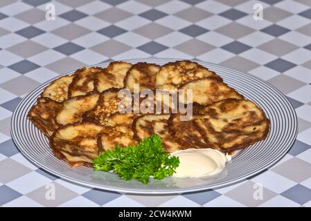 Deliziose frittelle di patate e zucchine con panna acida e fresche prezzemolo su sfondo grigio Foto Stock