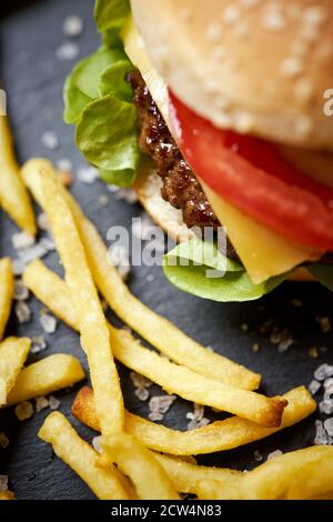 cheeseburger circondato da patatine fritte su un tavolo nero Foto Stock