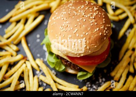 cheeseburger circondato da patatine fritte su un tavolo nero Foto Stock