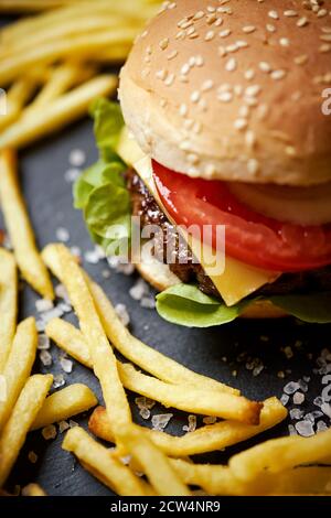 cheeseburger circondato da patatine fritte su un tavolo nero Foto Stock