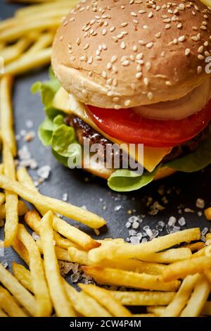 cheeseburger circondato da patatine fritte su un tavolo nero Foto Stock