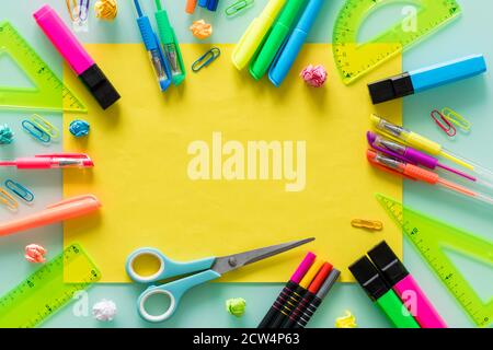 articoli per la scuola e l'ufficio, penne colorate, graffette, pennarelli, quadratini, un foglio di testo giallo vuoto al centro. Foto Stock