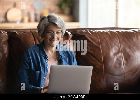 Donna anziana sorridente in occhiali che usa un computer portatile a casa Foto Stock