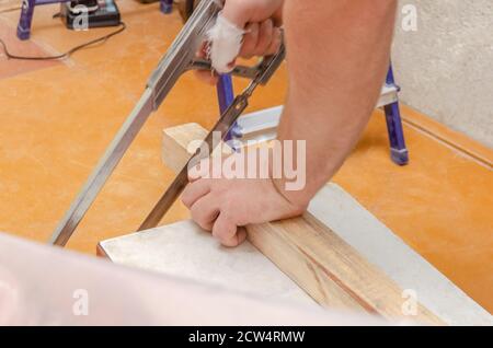 Primo piano delle mani di un uomo che taglia a. barra di legno con sega Foto Stock