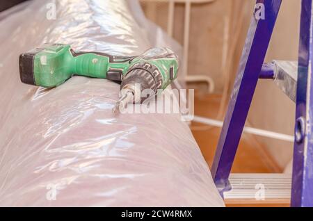 Vicino a un cacciavite elettrico su una superficie leggera, accanto ad essa è presente una scala. Il concetto di costruzione, riparazione e manutenzione della casa Foto Stock