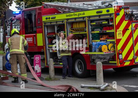 La donna Firefighter lancia il tubo con London Fire Brigade che assiste a un incendio in una strada residenziale, a sud di Londra, Inghilterra, Regno Unito Foto Stock