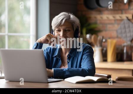 Donna anziana intelligente in cuffia: Guarda il webinar sul notebook Foto Stock