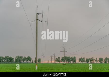 Linee di alimentazione ad alta tensione con poli elettrici al crepuscolo contro il cielo Foto Stock