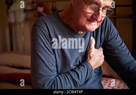 Uomo anziano con problemi di salute a casa stipando Chest in Dolore Foto Stock