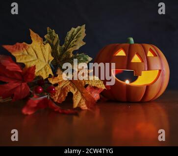 Zucca di Halloween con candela illuminata all'interno di esso accanto a foglie d'autunno colorate artificiali. Halloween e Vibes d'autunno. Foto Stock