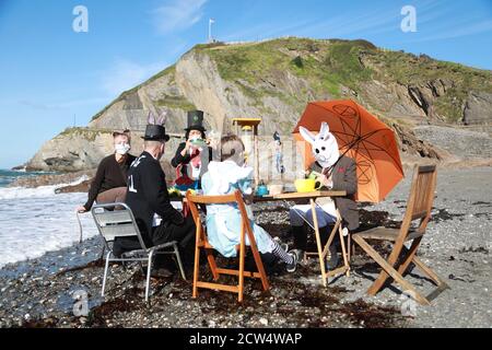 Ilfracombe, Nord Devon, Regno Unito. 27 Settembre 2020. Diversi membri del gruppo attivista del clima, la ribellione dell'estinzione, si sedettero attorno a un tavolo vestito da personaggi di Alice nel paese delle meraviglie, in attesa che la marea arriverà, il tema è stato quello di sottolineare ai curiosi che la marea non attende nessuno e che il tempo sta esaurendo per quanto riguarda le nostre azioni sul cambiamento climatico. Credit: Natasha Quarmby/Alamy Live News Foto Stock