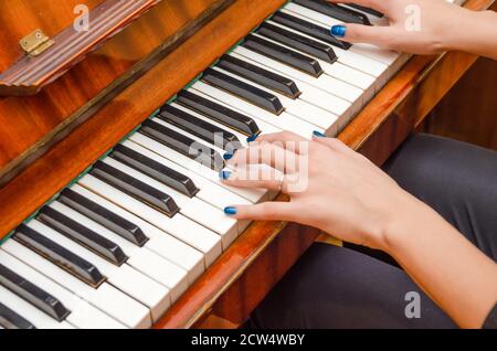 Mani di una pianista femminile con unghia blu polacca sui chiodi sulle chiavi di un pianoforte. Ragazza che suona il pianoforte. Foto Stock