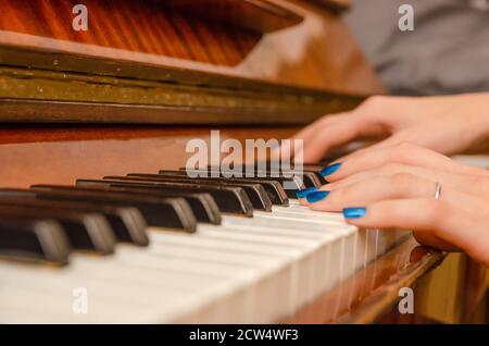 Mani di una pianista femminile con unghia blu polacca sui chiodi sulle chiavi di un pianoforte. Ragazza che suona il pianoforte. Foto Stock