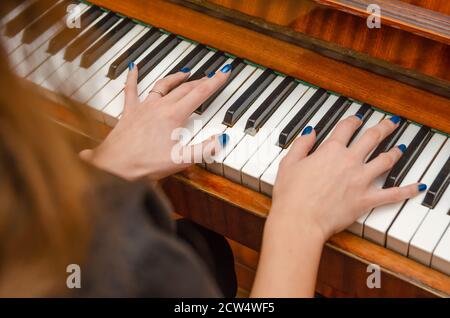 Mani di una pianista femminile con unghia blu polacca sui chiodi sulle chiavi di un pianoforte. Ragazza che suona il pianoforte. Foto Stock