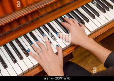 Mani di una pianista femminile con unghia blu polacca sui chiodi sulle chiavi di un pianoforte. Ragazza che suona il pianoforte. Foto Stock