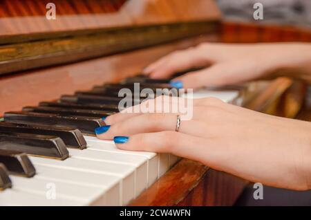 Mani di una pianista femminile con unghia blu polacca sui chiodi sulle chiavi di un pianoforte. Ragazza che suona il pianoforte. Foto Stock