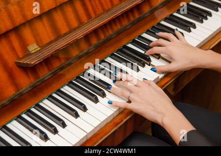 Mani di una pianista femminile con unghia blu polacca sui chiodi sulle chiavi di un pianoforte. Ragazza che suona il pianoforte. Foto Stock