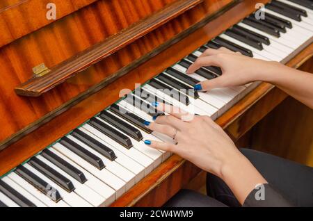 Mani di una pianista femminile con unghia blu polacca sui chiodi sulle chiavi di un pianoforte. Ragazza che suona il pianoforte. Foto Stock