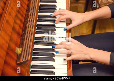 Mani di una pianista femminile con unghia blu polacca sui chiodi sulle chiavi di un pianoforte. Ragazza che suona il pianoforte. Foto Stock