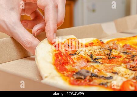 La mano femminile prende la pizza di carne con i funghi da un semplice primo piano della scatola di cartone Foto Stock