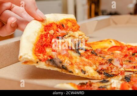 La mano femminile prende la pizza di carne con i funghi da un semplice primo piano della scatola di cartone Foto Stock