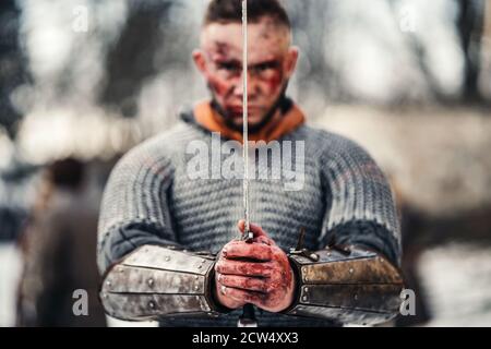 Giovane uomo forte in costume da guerriero medievale tiene una spada nelle mani proprio di fronte al viso. Concetto di guerra e storia. Foto Stock