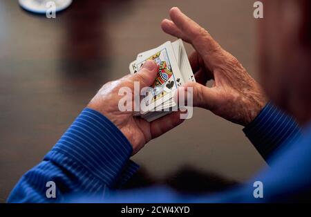 Primo piano di Senior Man a casa seduto al tavolo Mazzo di rimescolamento e carte da gioco Foto Stock