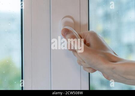 La mano femmina chiude la finestra con gocce sul vetro in una giornata di pioggia nuvolosa Foto Stock