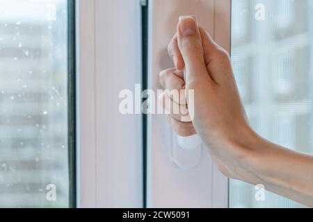 La mano femmina apre una finestra con gocce sul vetro in una giornata di pioggia nuvolosa Foto Stock