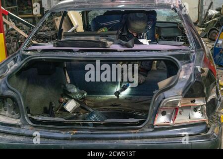 Auto dopo un incidente sulla linea di assemblaggio. Il meccanico esamina la vettura. Smontaggio, riparazione della vettura. Vista posteriore di un'auto semi-assemblata in una scatola. Foto Stock