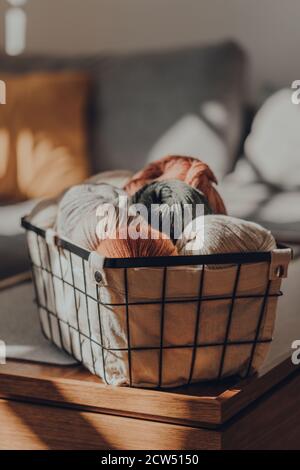 Palle di filato colorato di terra all'interno di un cesto su un tavolo all'interno di un appartamento, luce solare dalla finestra su di esso, fuoco selettivo. Foto Stock