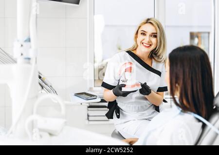 Dentista piuttosto femminile che spiega il modo di trattamento sulla protesi dentaria per il paziente in clinica Foto Stock