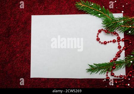 Foglio bianco di carta giace su uno sfondo morbido Borgogna con decorazioni natalizie. Sfondo di Natale con spazio di copia Foto Stock