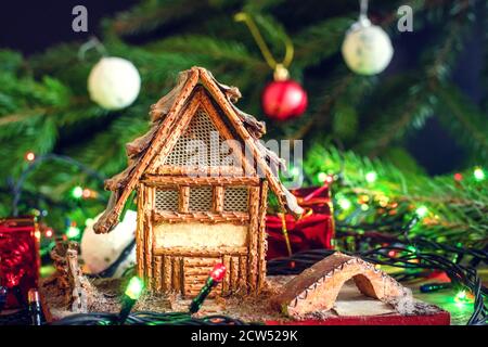Bellissimo sfondo di Natale, biglietto d'auguri. Una piccola casa si erge sullo sfondo di un albero di Natale, primo piano decorazioni di Natale. Foto Stock