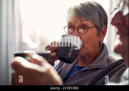 La coppia anziana si rilassa e chiacchiera insieme sul divano a casa Con bevanda calda Foto Stock